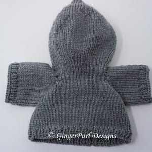 Puede incluir: Un su&eacute;ter con capucha gris tejido con mangas. El su&eacute;ter est&aacute; hecho de un hilo grueso y tiene un dobladillo y pu&ntilde;os acanalados. La capucha tiene punta en la parte superior. El texto "&copy; GingerPurl Designs" es visible en la parte inferior.