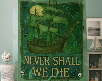 Op de afbeelding: Groene deken met een spookachtig piratenschipontwerp en de tekst "NEVER SHALL WE DIE". Het kunstwerk bevat een volle maan, bliksem en een schedel. De deken wordt door een persoon vastgehouden.