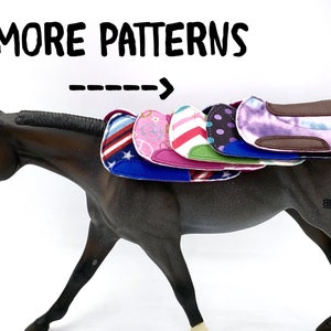 May include: A brown horse figurine with several colorful saddle pads. The saddle pads feature various patterns, including stars and stripes, pink hearts, and polka dots. The text "MORE PATTERNS" is above the horse.