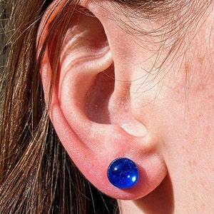 May include: A pair of blue glass earrings with a sparkly finish. The earrings are round and have a smooth surface.