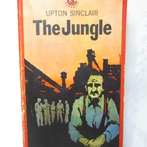 May include: Vintage paperback book cover for "The Jungle" by Upton Sinclair. The cover features a man with a mustache and suspenders, set against an industrial backdrop. The title is in large orange letters, with the publisher's logo at the top.