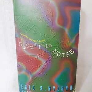May include: A paperback book titled "Signal to Noise" with a colorful cover. The cover features a green background with red, blue, and purple abstract designs and the author's name, Eric S. Nylund.