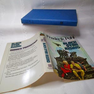 Puede incluir: Se muestra un libro abierto y un libro cerrado. El libro abierto muestra texto, con el t&iacute;tulo "Black Star Rising" y "Sudden Transition". La portada del libro abierto presenta una ilustraci&oacute;n colorida. El libro cerrado es azul.