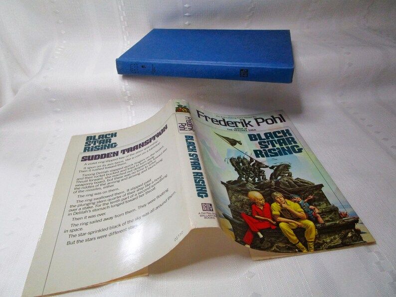 Puede incluir: Se muestra un libro abierto y un libro cerrado. El libro abierto muestra texto, con el t&iacute;tulo "Black Star Rising" y "Sudden Transition". La portada del libro abierto presenta una ilustraci&oacute;n colorida. El libro cerrado es azul.