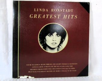 Könnte beinhalten: Ein Vintage-Vinyl-Schallplattenalbum mit dem Titel "Linda Ronstadt Greatest Hits". Das Albumcover ist in tiefem Burgunderrot mit goldfarbenen Buchstaben gehalten und zeigt ein rundes Porträt von Linda Ronstadt. Songtitel sind unten aufgeführt.