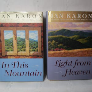 May include: Two hardcover books by Jan Karon. The book on the left is titled "In This Mountain" with a window scene. The book on the right is titled "Light from Heaven" with a mountain scene. Both books have a light blue background.