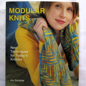 May include: A book cover titled "MODULAR KNITS" with a woman wearing a colorful knitted scarf. The book also says "New Techniques for Today's Knitters" by Iris Schreier. The scarf has blue, yellow, and orange sections.