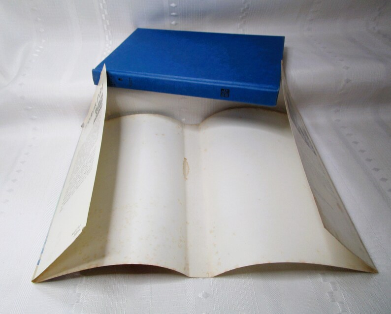 Puede incluir: Un libro azul de tapa dura descansa sobre un libro abierto con p&aacute;ginas envejecidas de color blanquecino. El libro abierto est&aacute; colocado para crear una forma de tienda de campa&ntilde;a, con el libro azul como &aacute;pice. Las p&aacute;ginas muestran signos de edad.