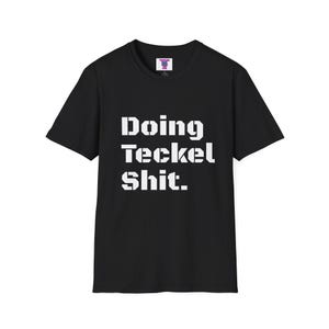 May include: A black short-sleeved t-shirt featuring the white text "Doing Teckel Shit." printed in a bold, blocky, stencil-style font across the center of the chest. The garment has a crew neckline and a standard fit with a small brand label at the neck.