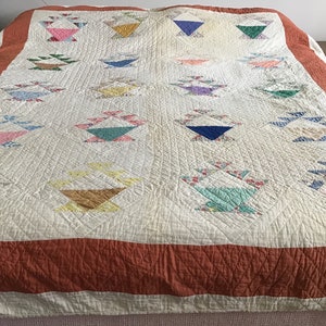 Puede incluir: Una colcha blanca con un borde rojo y un patrón de cestas de colores. La colcha está hecha de tela de retazos y está acolchada con un patrón de diamante.