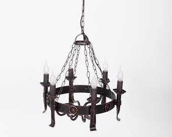 May include: A wrought iron chandelier with six faux candle lights. The fixture is suspended by a chain and features a circular design with decorative elements. The metal has a dark, rustic finish, and the lights have a warm glow.