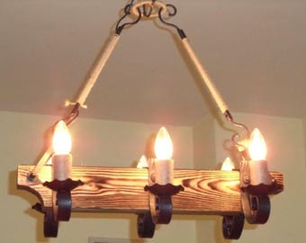 May include: A rustic chandelier with three candle-shaped lights. The fixture features a wooden beam with decorative metal accents and rope-wrapped supports. The lights are illuminated, casting a warm glow.