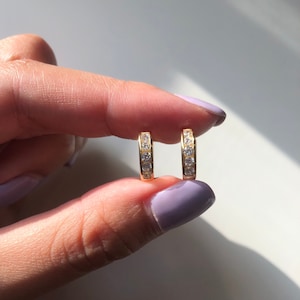 May include: A pair of gold hoop earrings with a row of clear cubic zirconia stones.
