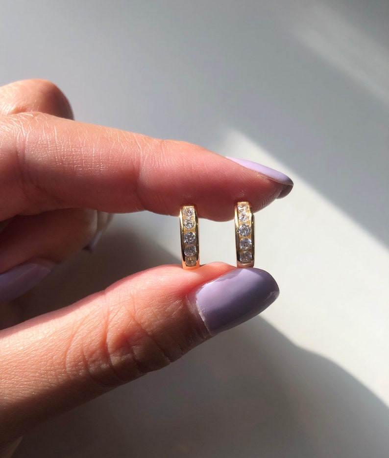 May include: A pair of gold hoop earrings with a row of clear cubic zirconia stones.