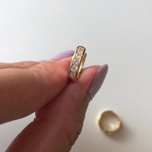 May include: A pair of gold hoop earrings with a row of clear cubic zirconia stones.