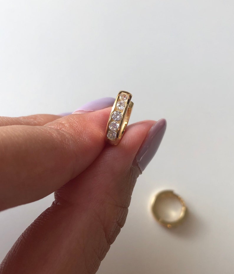 May include: A pair of gold hoop earrings with a row of clear cubic zirconia stones.