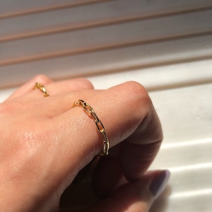 May include: A gold chain ring on a finger. The ring is made of small, linked oval shapes.