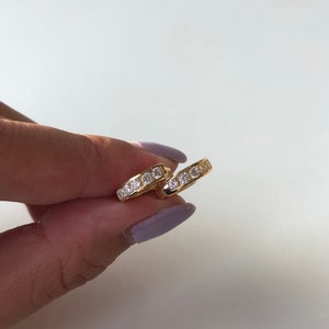 May include: A pair of gold hoop earrings with a row of clear cubic zirconia stones around the edge.