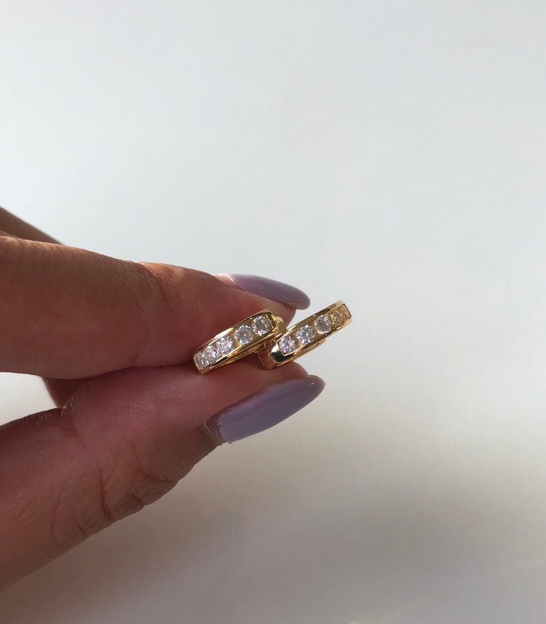 May include: A pair of gold hoop earrings with a row of clear cubic zirconia stones around the edge.