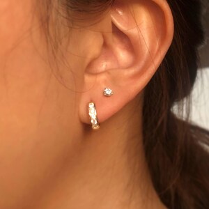 May include: A pair of gold hoop earrings with small clear stones set in the metal. The earrings are worn in the earlobe of a person.
