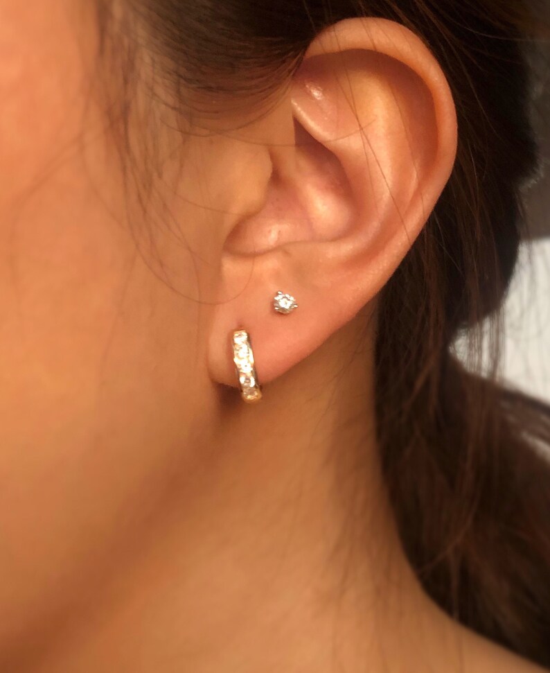 May include: A pair of gold hoop earrings with small clear stones set in the metal. The earrings are worn in the earlobe of a person.