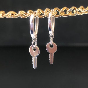 May include: A pair of silver key earrings with hoop-style posts. The keys have a simple design with a round keyhole and a straight, serrated edge.