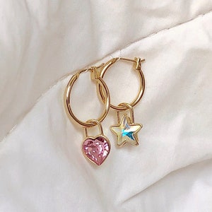 May include: Gold hoop earrings with a pink heart and a clear star charm hanging from each hoop.