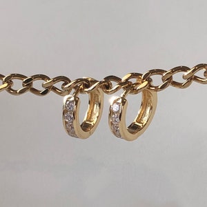 May include: A pair of gold hoop earrings with a row of small clear stones around the edge.
