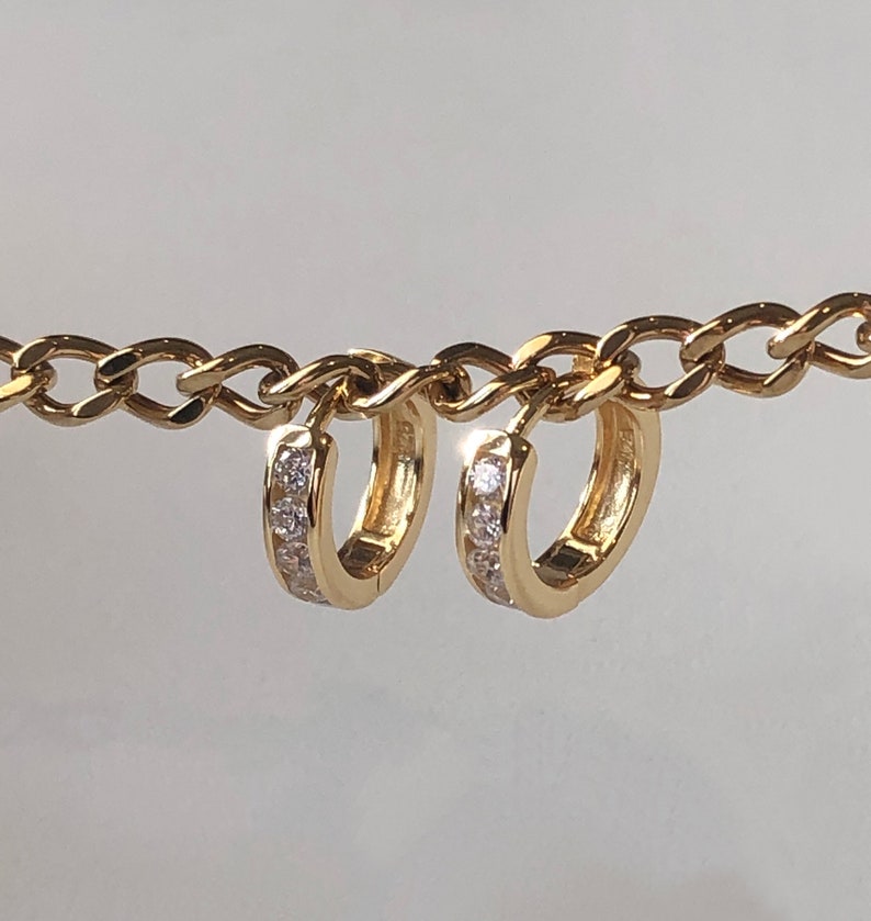 May include: A pair of gold hoop earrings with a row of small clear stones around the edge.