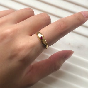 May include: A gold ring with a small red heart-shaped stone set in the center.