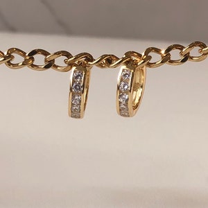 May include: A pair of gold hoop earrings with a single row of clear cubic zirconia stones.
