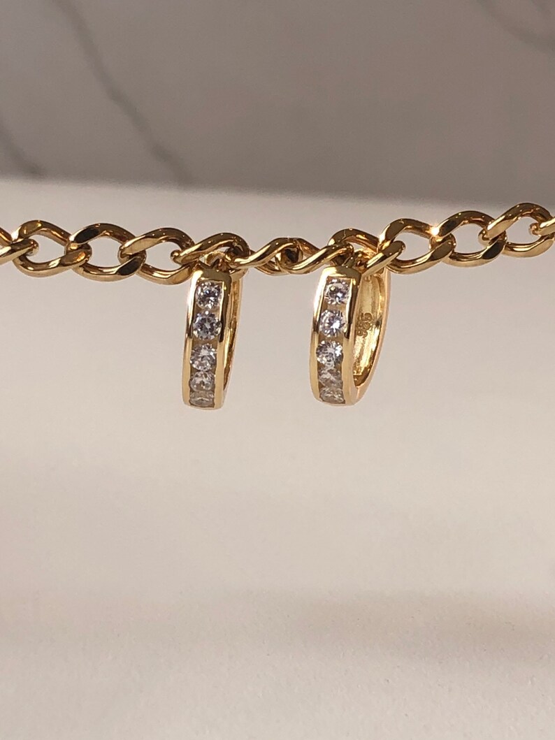 May include: A pair of gold hoop earrings with a single row of clear cubic zirconia stones.