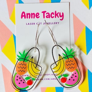 May include: A pair of clear acrylic hoop earrings with a colorful fruit design. The earrings feature a watermelon, pineapple, banana, and cherry. The earrings are laser cut and made by Anne Tacky.