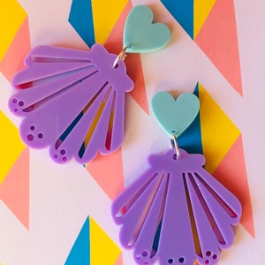 May include: A pair of purple shell earrings with a light blue heart charm on each earring.