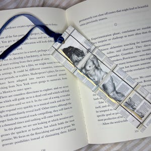 May include: Handmade bookmark with a blue ribbon, featuring a grayscale image of a nude figure. The bookmark is constructed from small, book-page squares, creating a unique, artistic design.