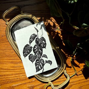 K&ouml;nnte beinhalten: Ein Schwarz-Wei&szlig;-Druck einer Monstera-Pflanze auf wei&szlig;em Hintergrund. Der Druck befindet sich auf einem silbernen Tablett mit goldfarbenem Rand.