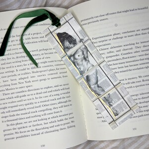 May include: A handmade bookmark featuring a classical nude figure, constructed from small, book-page squares. The bookmark has a green velvet ribbon attached, resting on an open book.