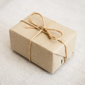 Op de afbeelding: Een bruine papieren cadeaudoos gebonden met touw. De doos is ingepakt in bruin papier en gebonden met touw, wat een eenvoudige en rustieke uitstraling cre&euml;ert.
