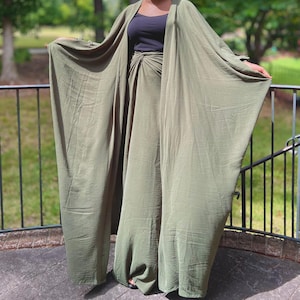 May include: An olive green, flowing outfit consisting of a long, open-front cardigan and matching wide-leg pants. The outfit is worn over a black top. The fabric appears to be lightweight and textured, suitable for warmer weather.