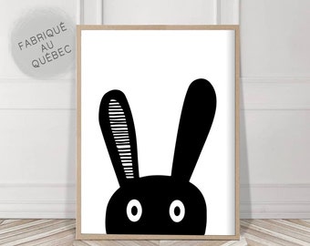 May include: Framed art print featuring a minimalist black and white bunny design. The bunny's head and ears are depicted with simple shapes and lines. The print is in a light wood frame and includes the text "atelier cartouche".