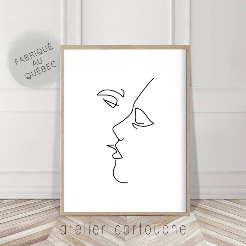 May include: A framed minimalist art print featuring a black line drawing of two faces in profile, appearing to be kissing. The print is in a light wood frame. The text "atelier cartouche" is at the bottom.