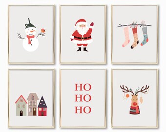 May include: Six framed Christmas-themed art prints. The prints feature a snowman, Santa Claus, hanging stockings, colorful houses, the text "HO HO HO", and a reindeer with antlers. Each print has a gold frame and a light gray background.