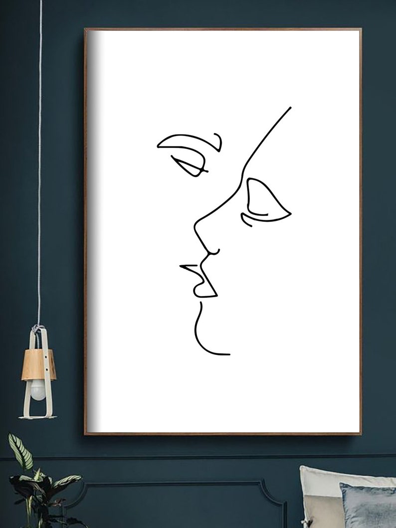 May include: A framed minimalist art print featuring a black line drawing of two faces in profile, appearing to be kissing. The artwork is set against a white background, with a simple, elegant aesthetic. The frame is a dark brown color.
