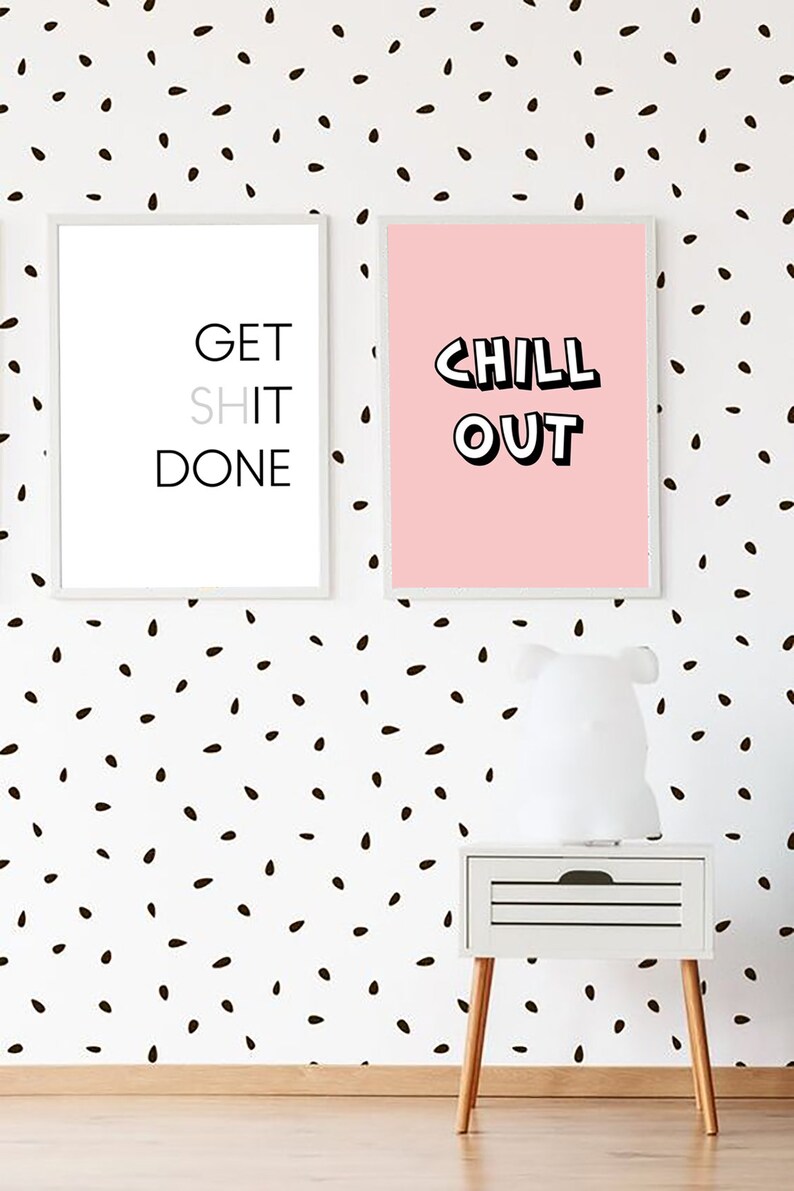Może przedstawiać: Dwa oprawione wydruki z motywującymi frazami wiszą na białej ścianie z czarnymi plamkami. Jeden m&oacute;wi "GET SHIT DONE", drugi "CHILL OUT". Poniżej znajduje się biała szafka nocna z drewnianymi nogami.