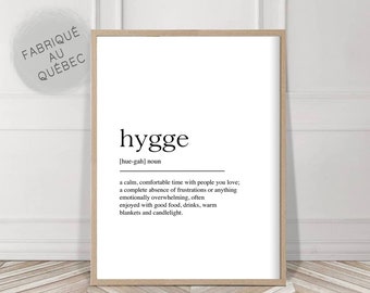 Könnte beinhalten: Ein gerahmter Druck mit dem Wort "hygge" in Schwarz, zusammen mit seiner Aussprache und Definition. Die Definition beschreibt eine ruhige, angenehme Zeit mit geliebten Menschen. Der Druck ist in einem hellen Holzrahmen, mit dem Text "FABRIQUÉ AU QUÉBEC" in einem Kreis.