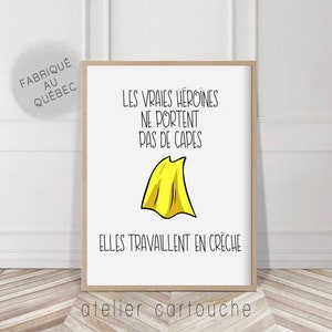 May include: Framed art print with the text "LES VRAIES HÉROÏNES NE PORTENT PAS DE CAPES ELLES TRAVAILLENT EN CRÈCHE" and a yellow cape illustration. The print is in a wooden frame and has a white background. The text "FABRIQUÉ AU QUÉBEC" is in a circle.