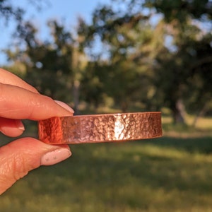 K&ouml;nnte beinhalten: Ein geh&auml;mmertes Kupferarmband mit gl&auml;nzender Oberfl&auml;che. Das Armband ist ein schlichtes, massives Band mit einer strukturierten Oberfl&auml;che.