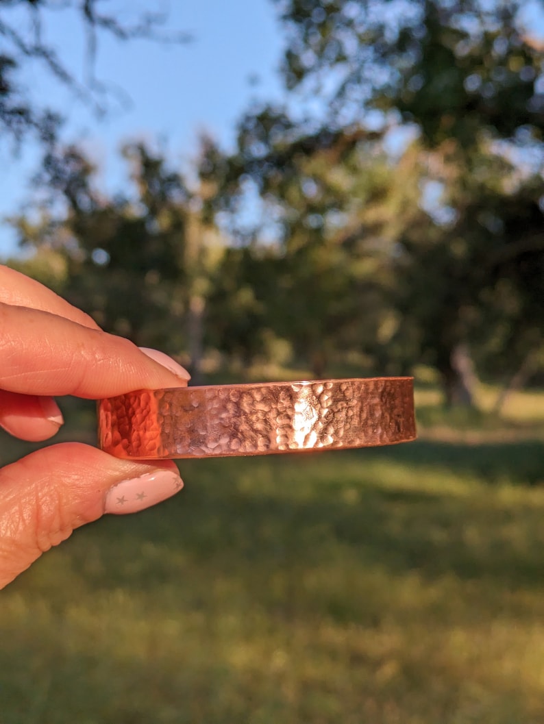 K&ouml;nnte beinhalten: Ein geh&auml;mmertes Kupferarmband mit gl&auml;nzender Oberfl&auml;che. Das Armband ist ein schlichtes, massives Band mit einer strukturierten Oberfl&auml;che.