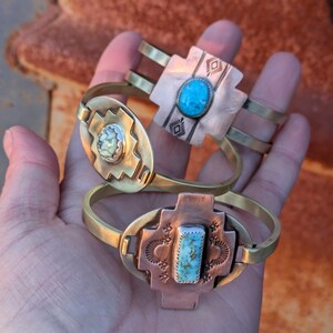 May include: Two brass bracelets with turquoise stones. The bracelets are decorated with geometric patterns and have a southwestern style.