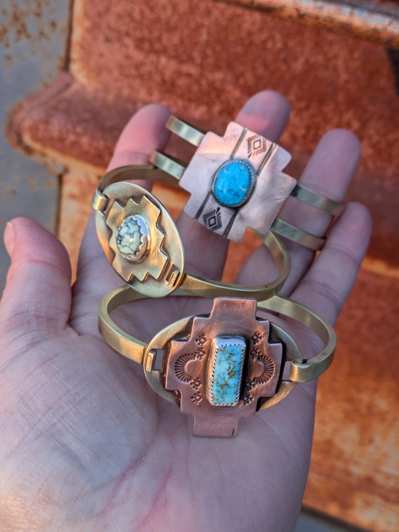 May include: Two brass bracelets with turquoise stones. The bracelets are decorated with geometric patterns and have a southwestern style.